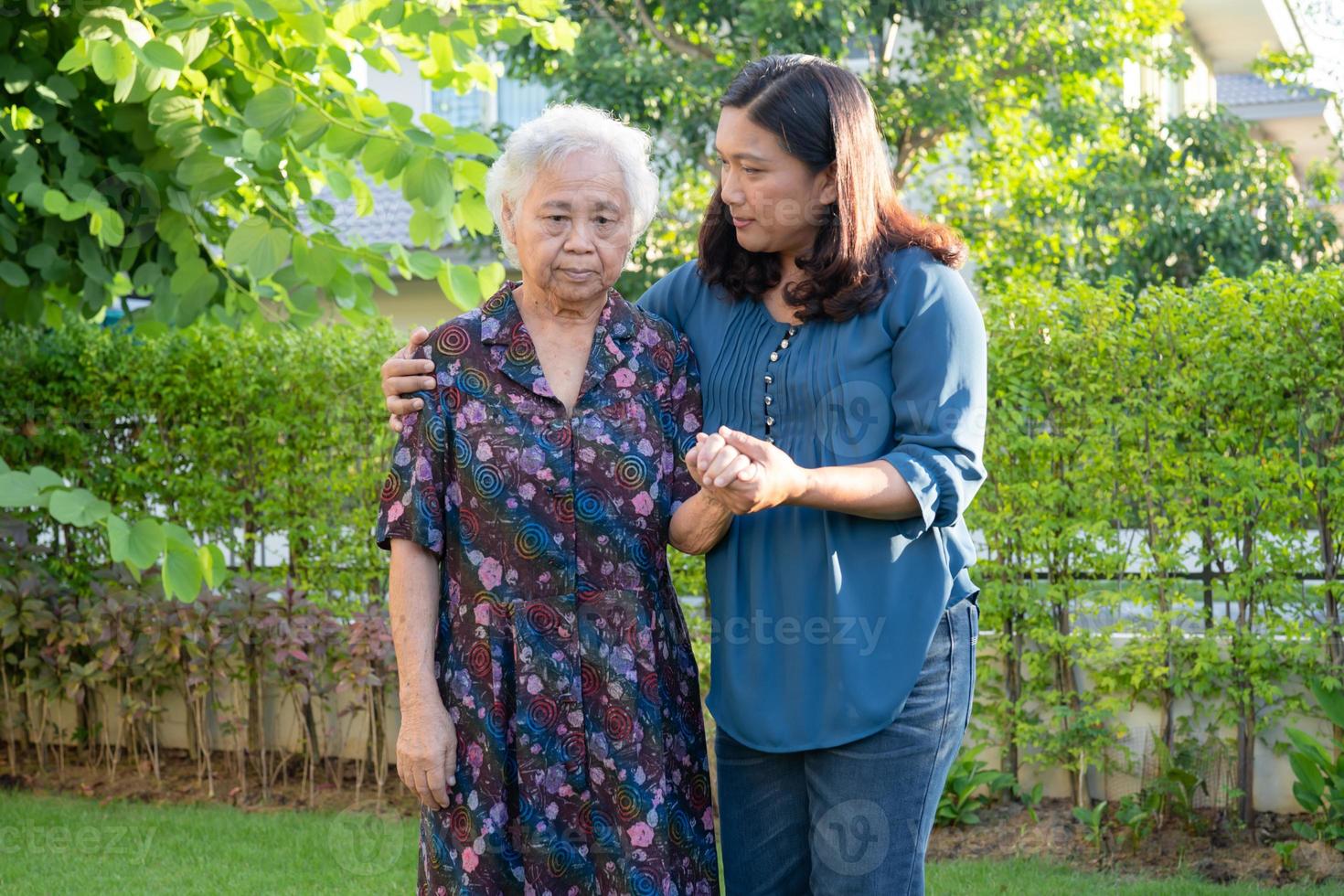 Caregiver help Asian elderly woman while walking with happy in nature park. photo
