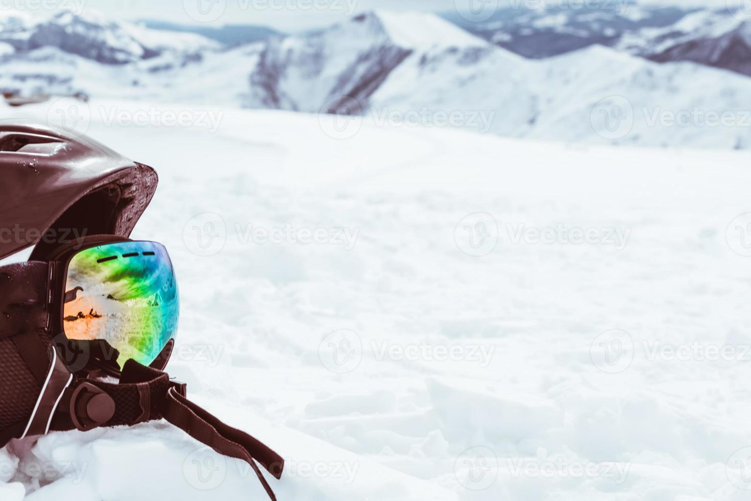 Casco negro con gafas de esquí en la nieve con fondo de paisaje de montañas nevadas blancas foto