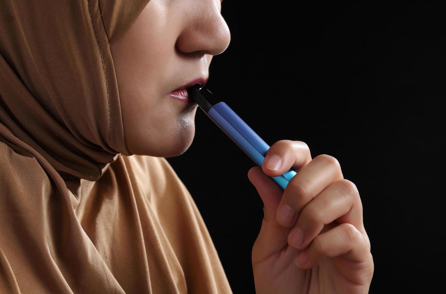 Close up young muslim woman smoking e-cigarette on black background photo