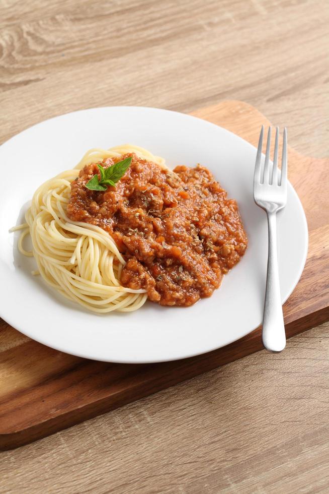 Cerrar un tenedor con espaguetis y salsa roja en un plato blanco sobre la tabla de cortar foto