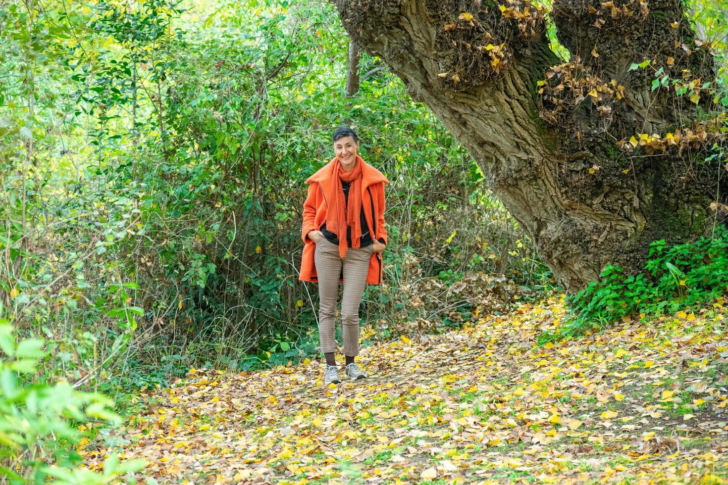 Mujer de mediana edad en abrigo naranja posando en el parque foto