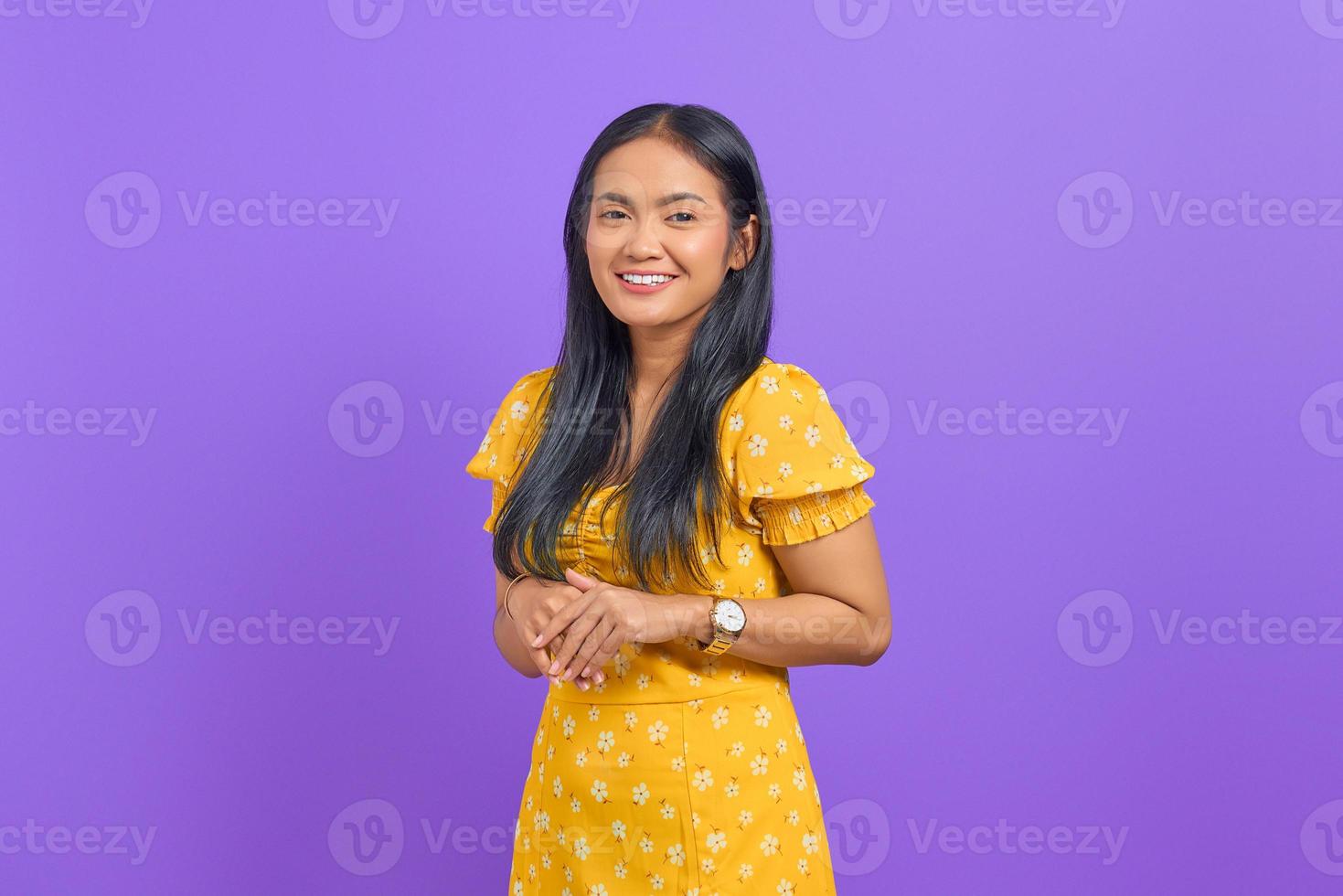 Smiling young Asian woman keeps hand together and feels optimistic on purple background photo