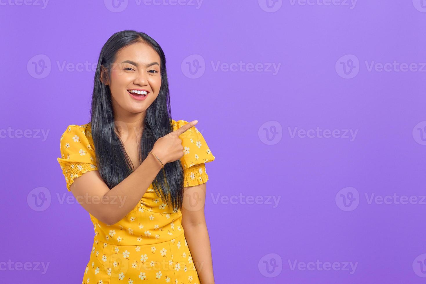 retrato, de, sonriente, joven, mujer asiática, señalar con el dedo, en, espacio de la copia, en, fondo púrpura foto