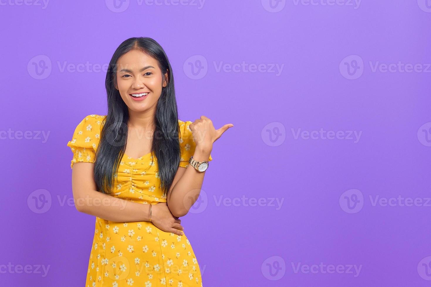 retrato, de, sonriente, joven, mujer asiática, señalar con el pulgar, en, copia, espacio, en, fondo púrpura foto