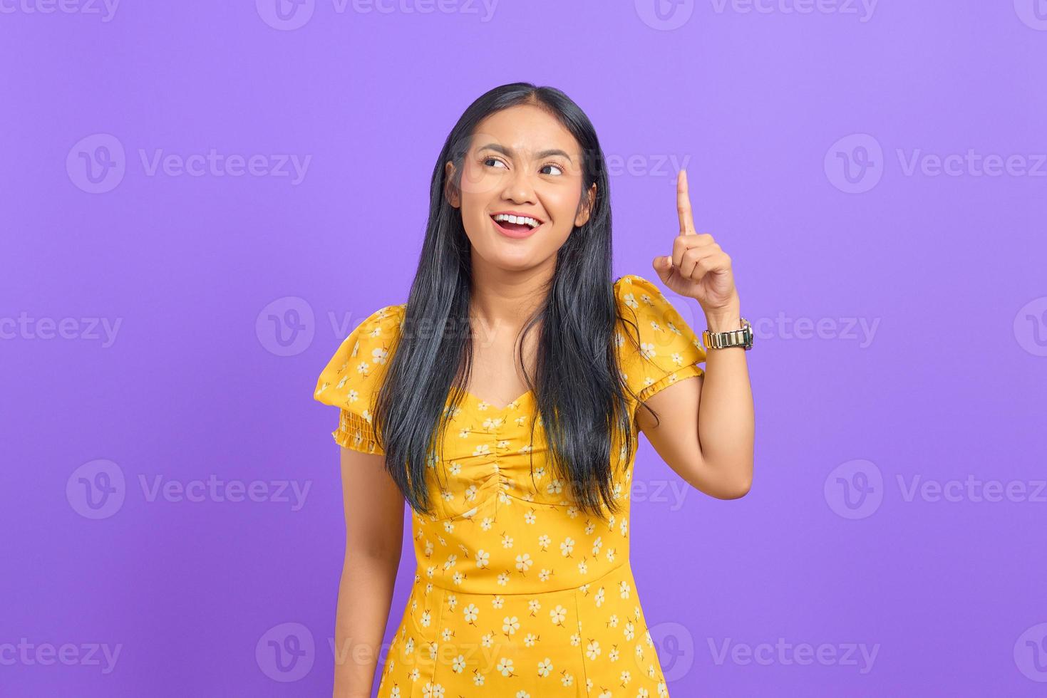 Smiling young Asian woman pointing fingers up and having an idea on purple background photo