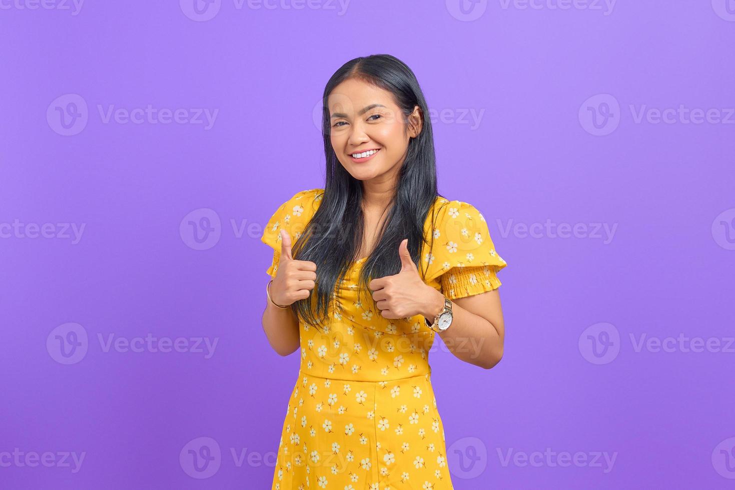 Retrato de mujer asiática joven sonriente que muestra los pulgares para arriba en la cámara sobre fondo púrpura foto