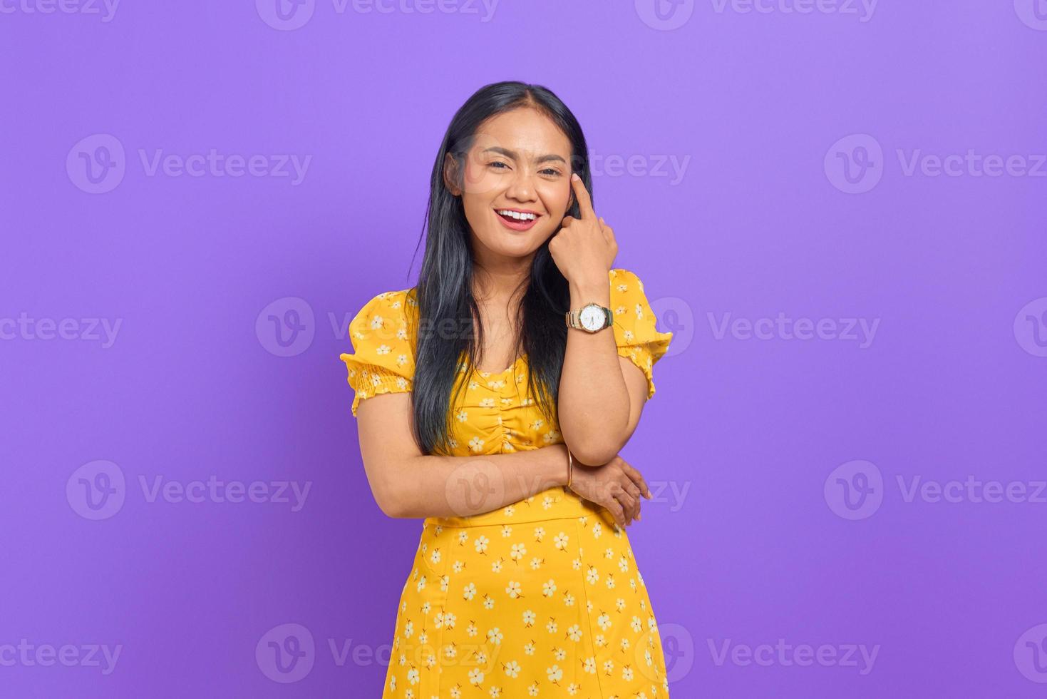 Smiling young Asian woman wearing yellow dress and looking confident on purple background photo