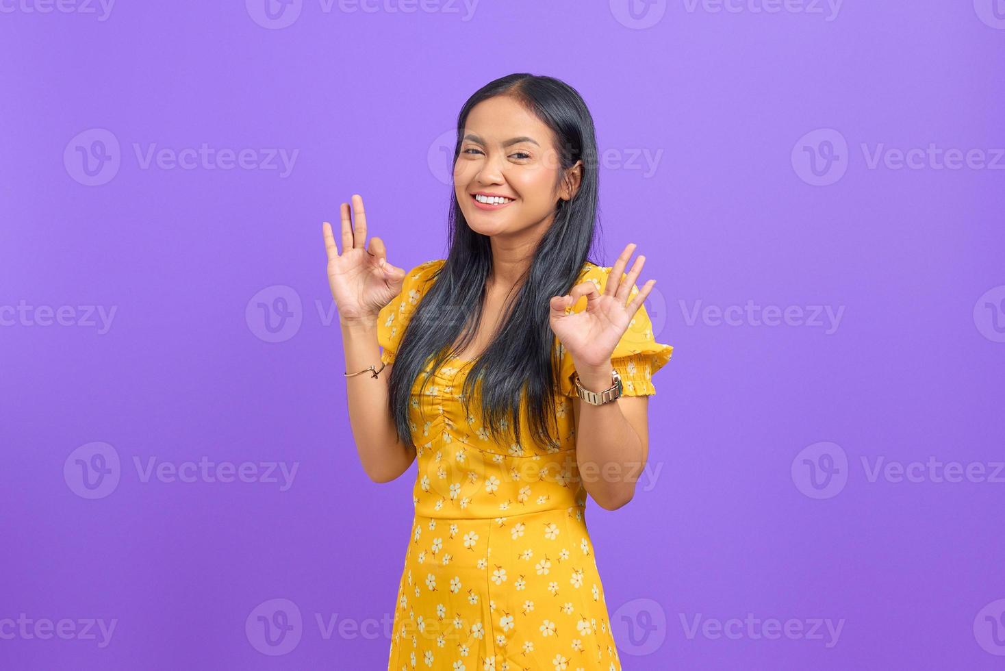 Cheerful young Asian woman makes okay gesture, demonstrates symbol of approval on purple background photo