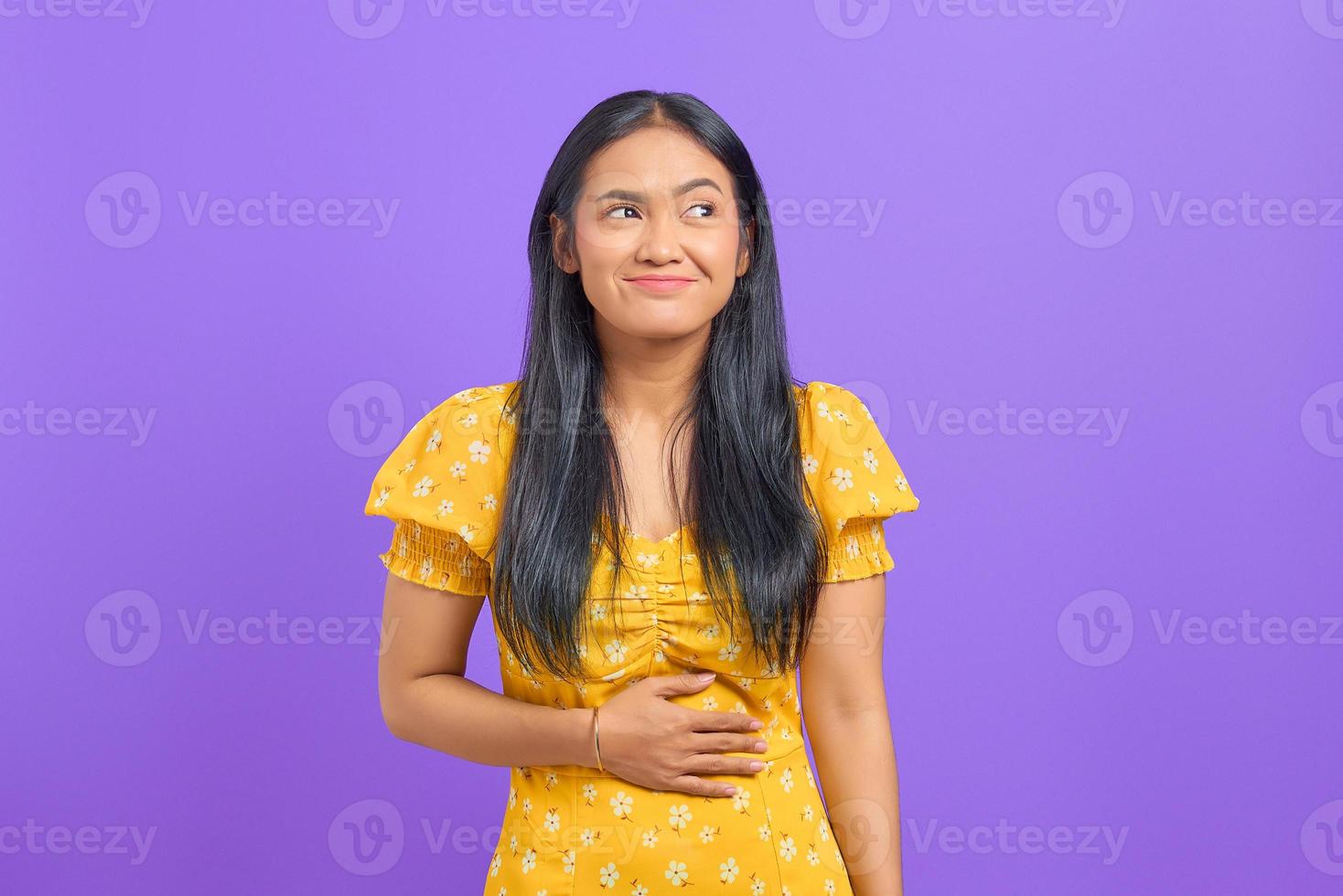 Young Asian woman keep hands on stomach and feel satiety after eating tasty on purple background photo