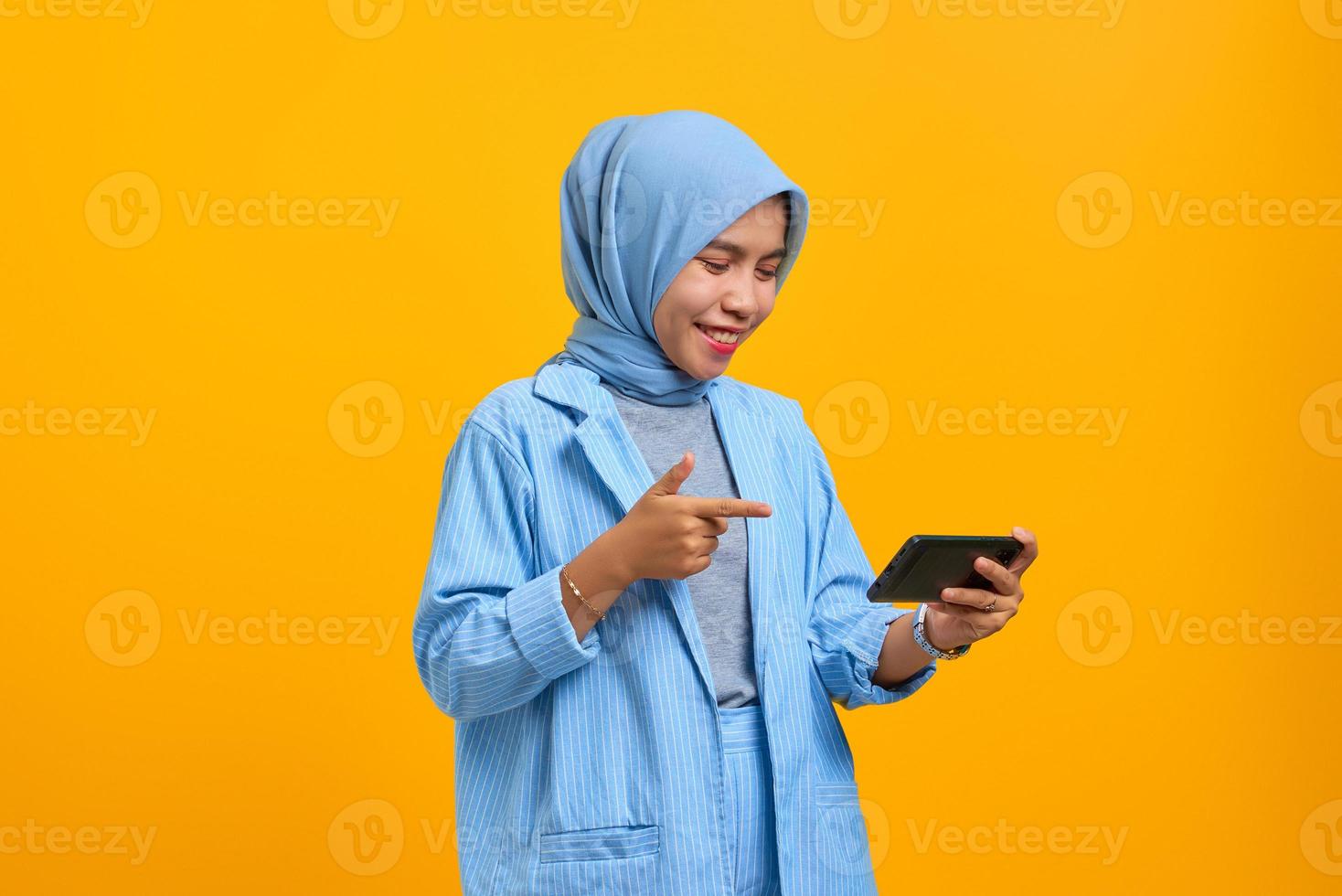 Cheerful young Asian woman playing video game on mobile phone isolated over yellow background photo