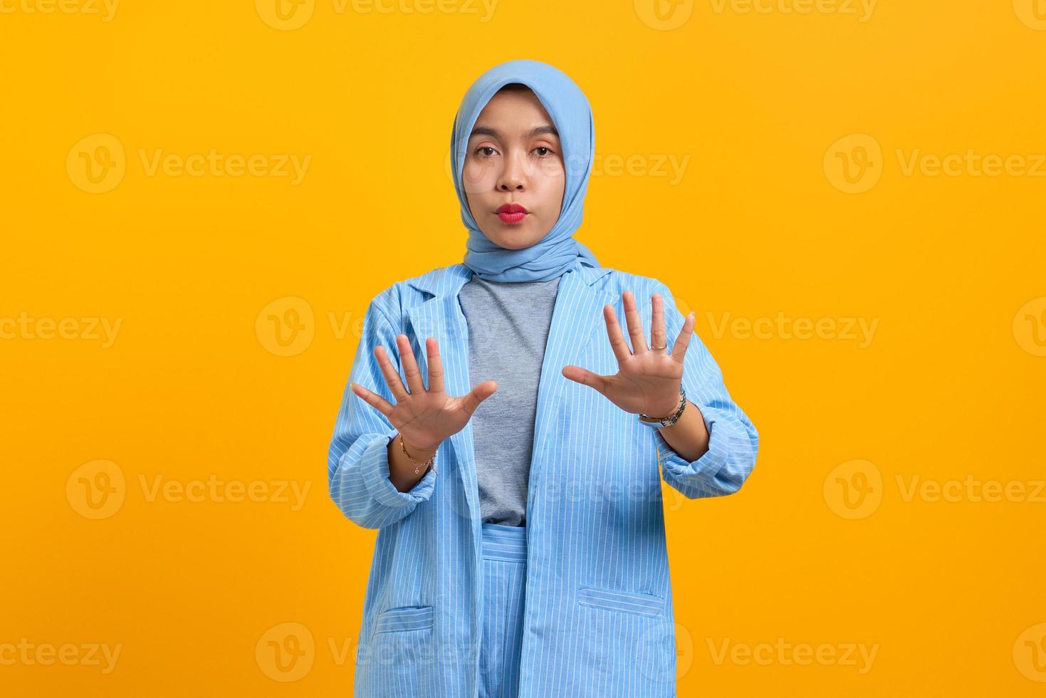 Joven mujer asiática haciendo gesto de parada con las palmas de las manos aisladas sobre fondo amarillo foto