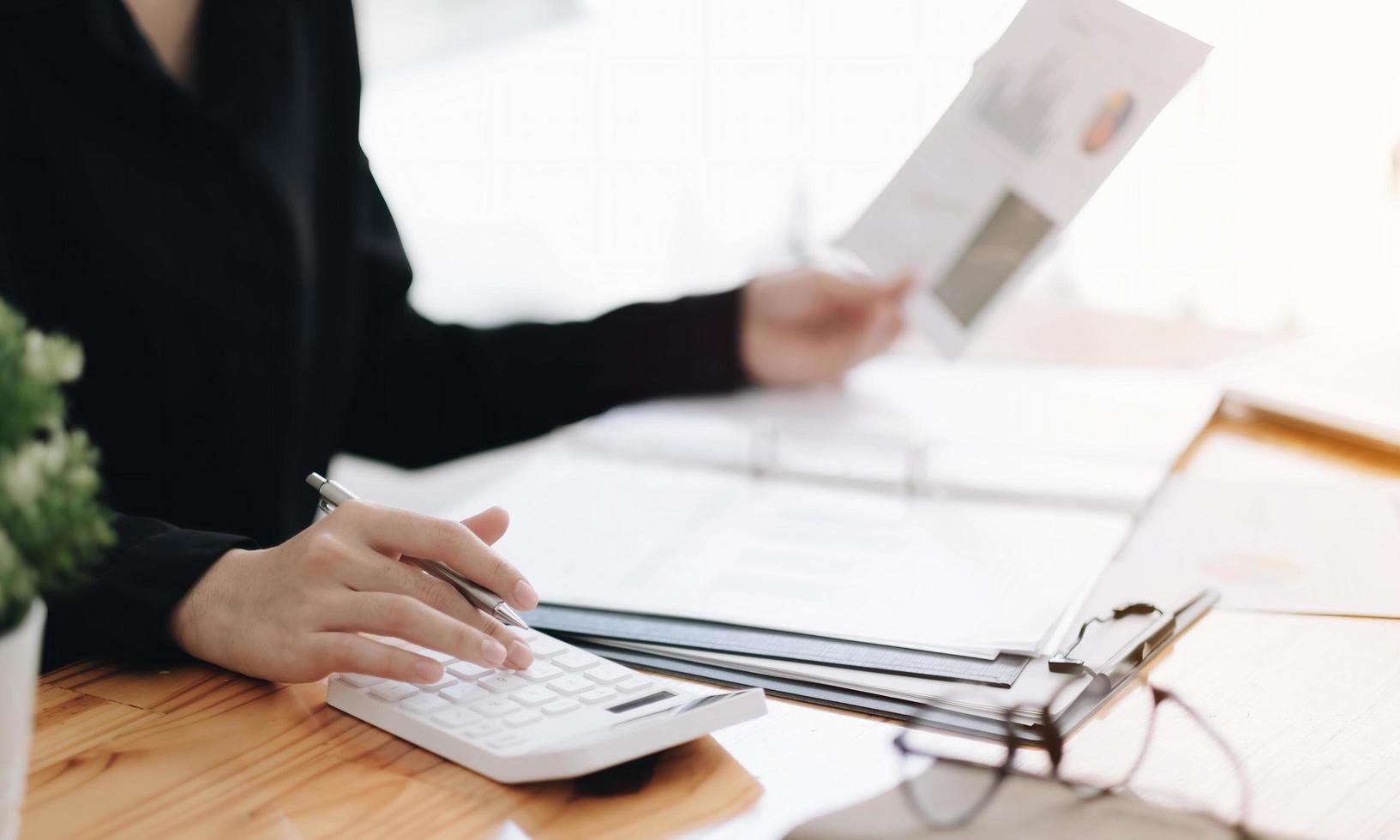 Close up of businesswoman or accountant hand holding pen working on calculator to calculate business data, accountancy document and laptop computer at office, business concept photo