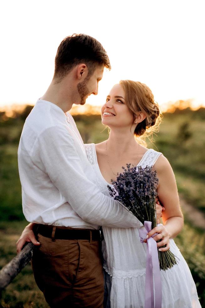 girl in a white sundress and a guy in a white shirt on a walk at sunset with a bouquet photo