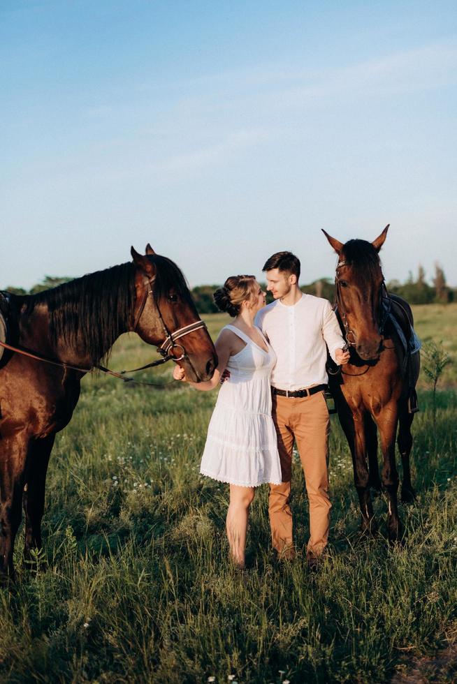 girl in a white sundress and a guy in a white shirt on a walk with brown horses photo