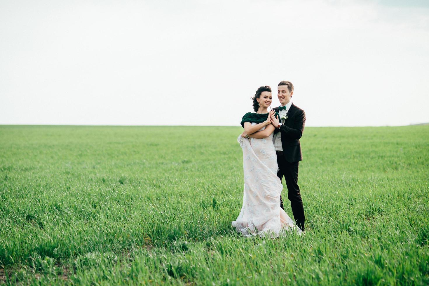 the groom in a brown suit and the bride in an ivory-colored dress on a green field photo