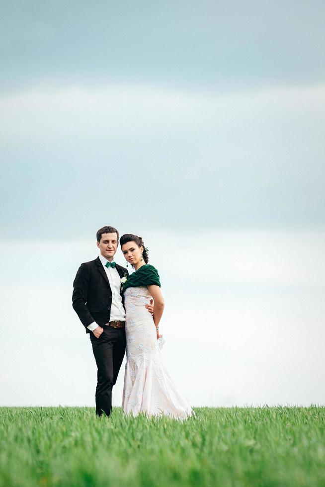 el novio con un traje marrón y la novia con un vestido color marfil en un campo verde foto