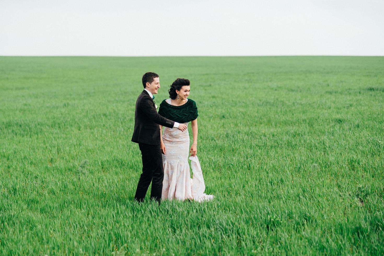 the groom in a brown suit and the bride in an ivory-colored dress on a green field photo