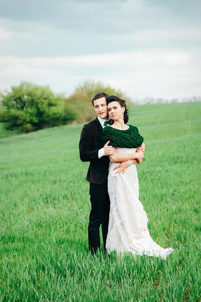 el novio con un traje marrón y la novia con un vestido color marfil en un campo verde foto