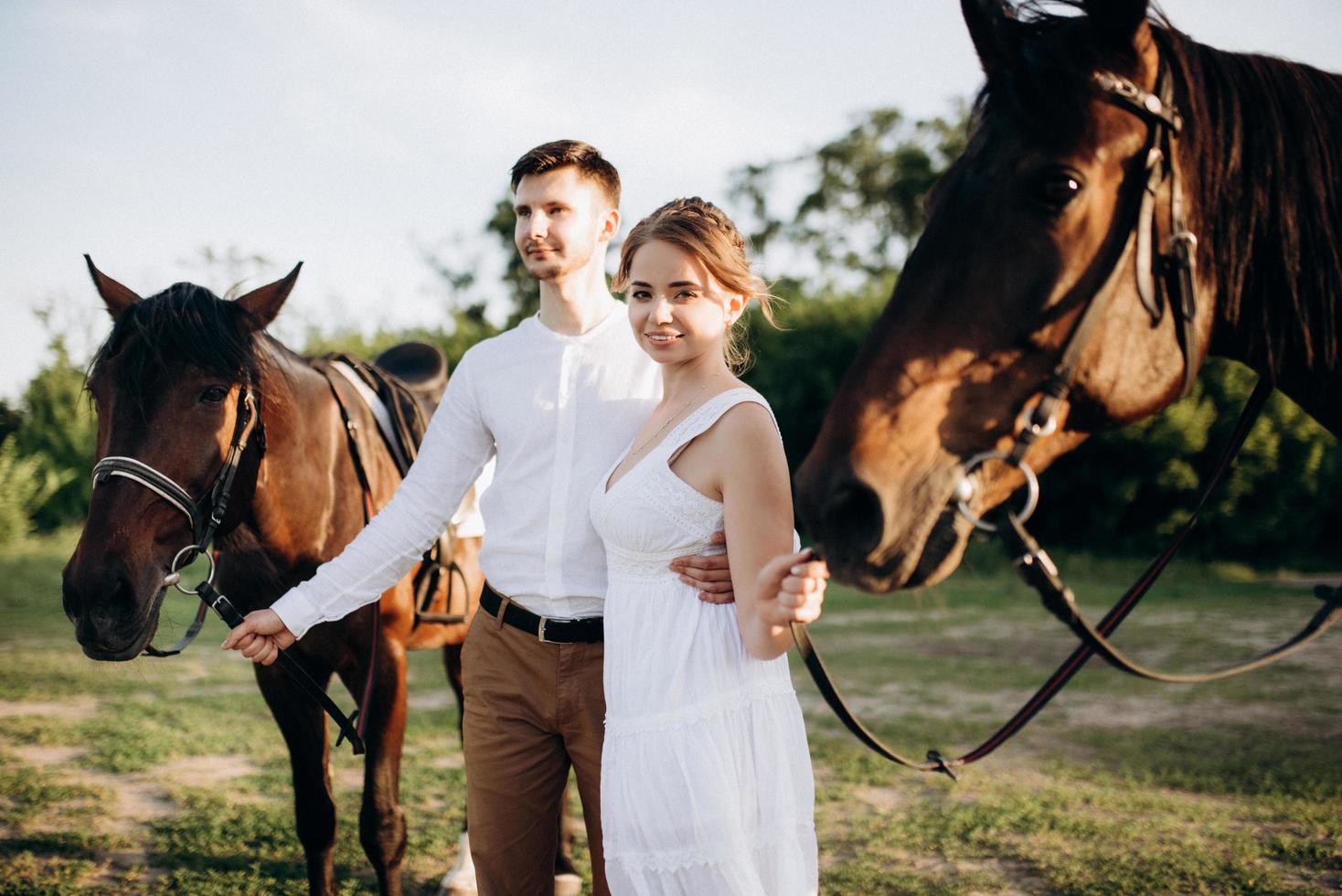 girl in a white sundress and a guy in a white shirt on a walk with brown horses photo