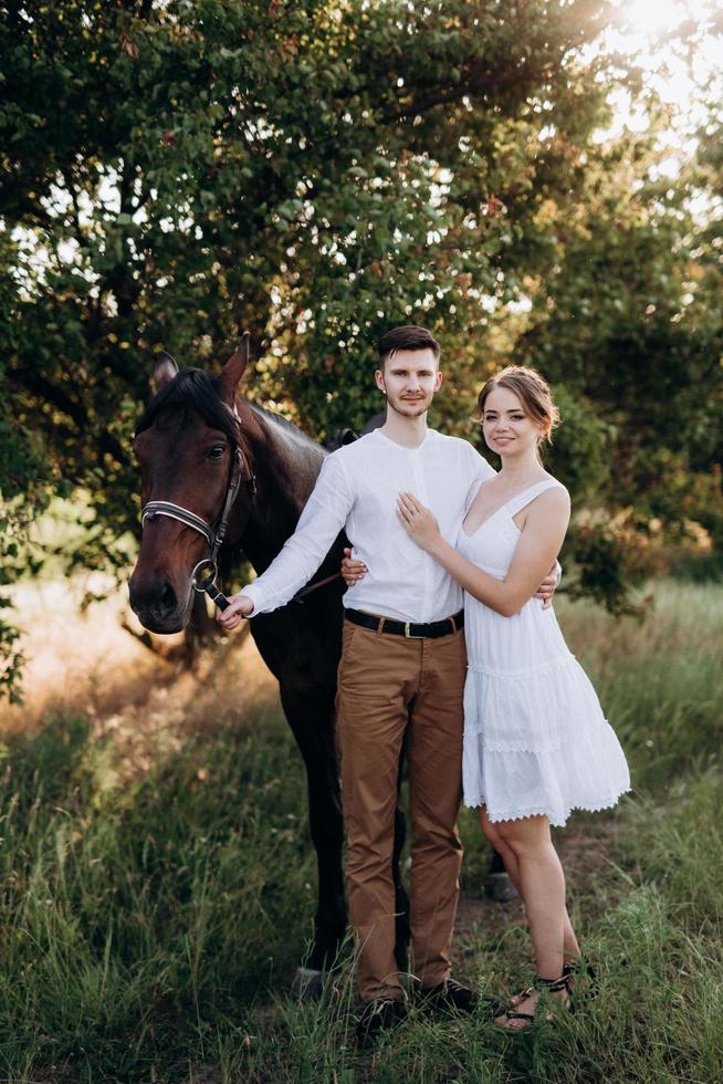 girl in a white sundress and a guy in a white shirt on a walk with brown horses photo