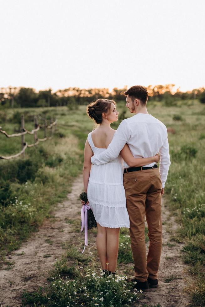 girl in a white sundress and a guy in a white shirt on a walk at sunset with a bouquet photo
