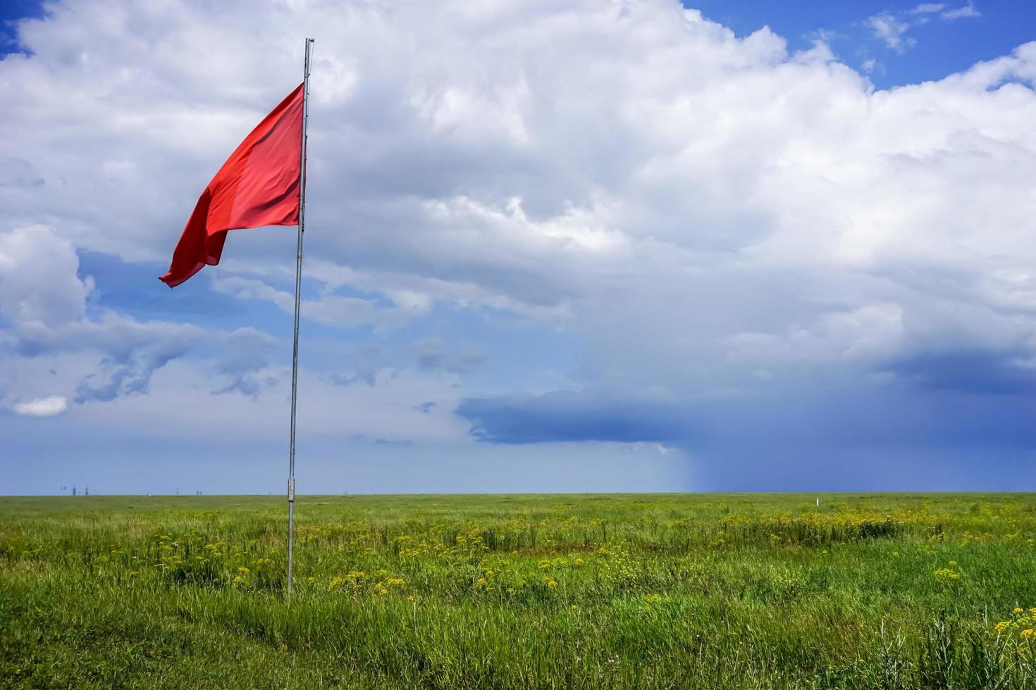The steppe is covered with bright green grass with a flagpole and red flag against the blue sky and white clouds photo