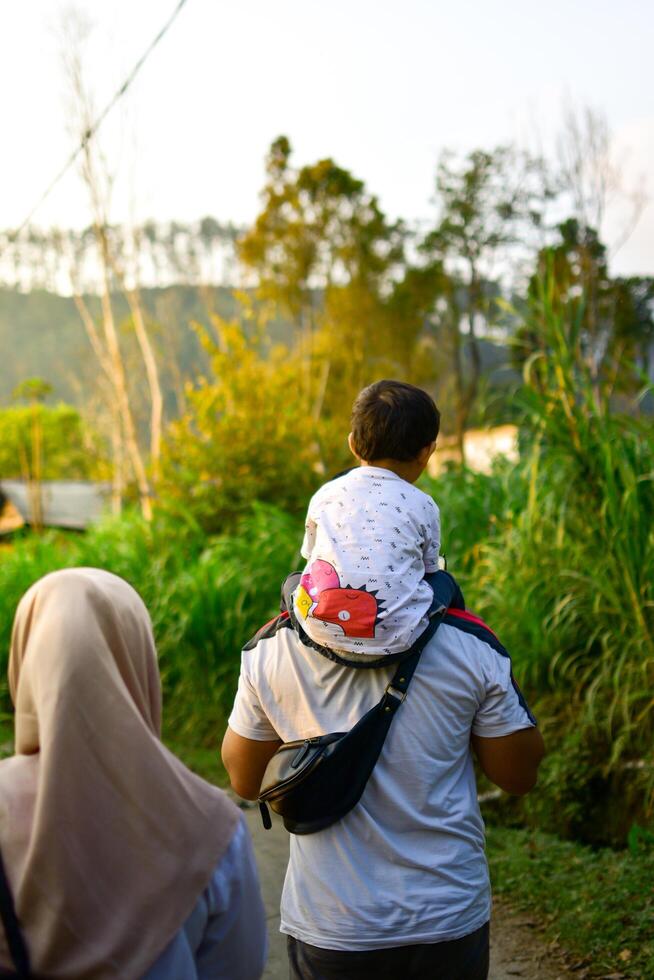 Ponorogo, Indonesia 2021 - Family strolling around. Dad carrying son. photo