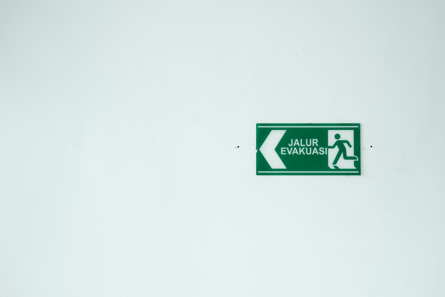 the evacuation route sign in green color is hanging on a white wall. the essential sign of the public places. photo