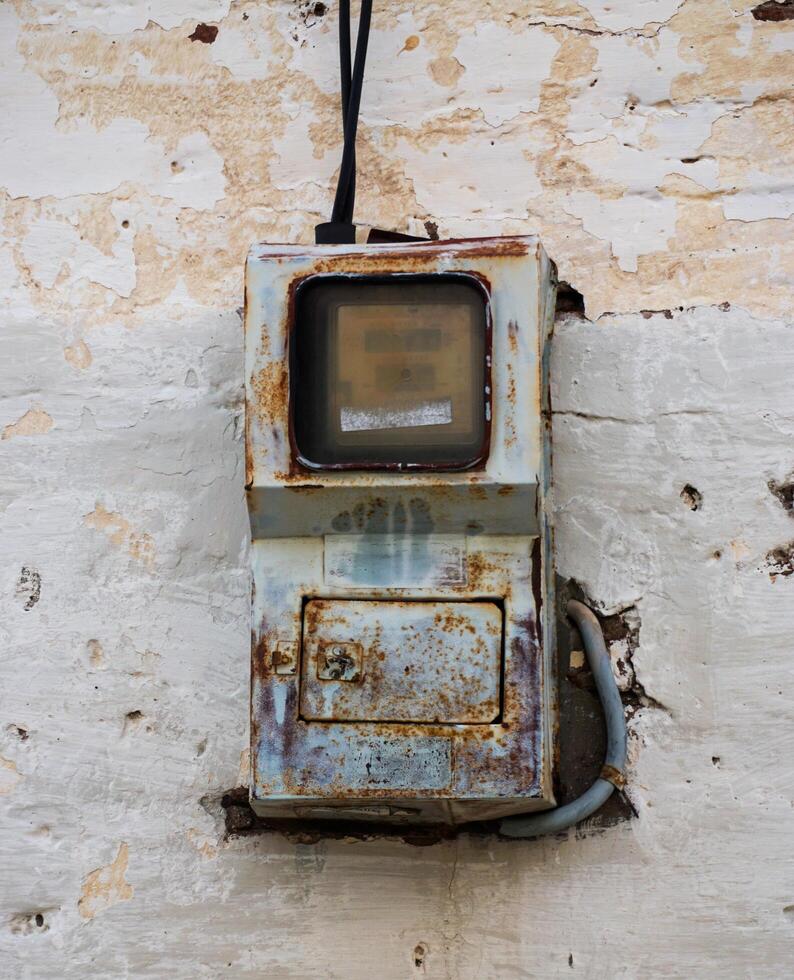 an old electric meter on the wall covered with rusty iron. a tool in the household to measure the electricity consumed. photo