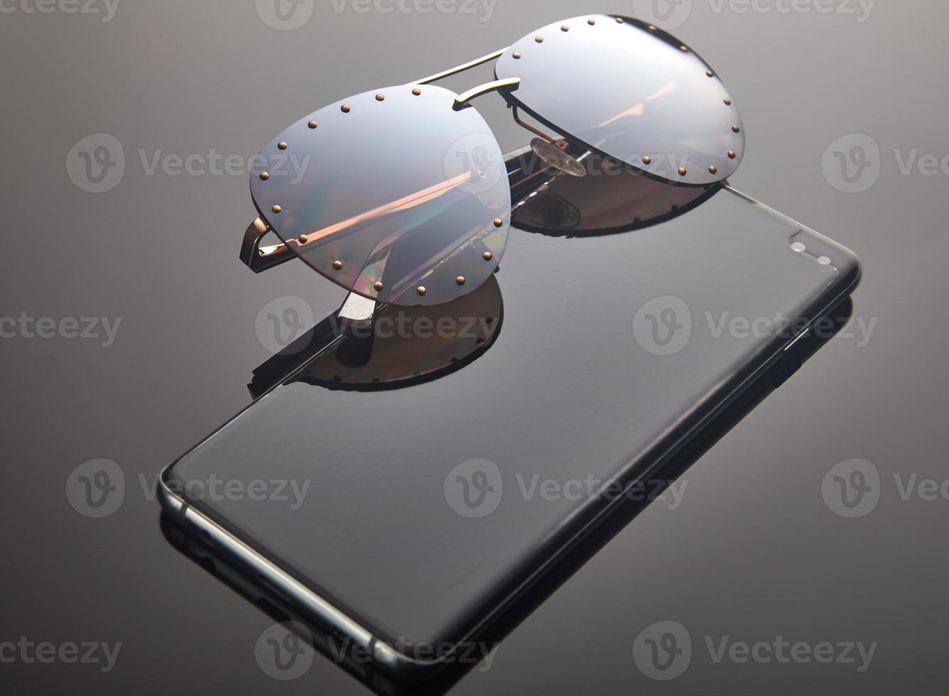 gafas de sol de mujer y smartphone sobre un fondo gris degradado con reflejo. lugar para el texto foto