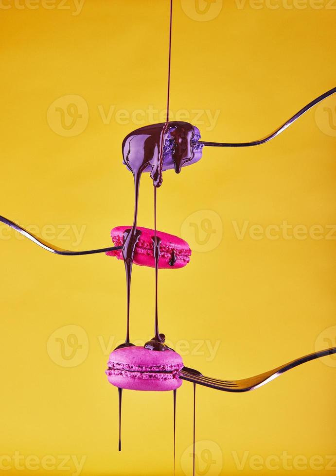 Multi-colored Macaron on forks with chocolate flowing from above on a yellow background photo