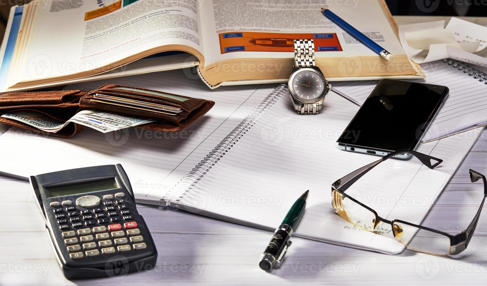 Business concept. Side view glasses, smartphone, notebook and pen, clock and calculator, purse on wooden table. Selective focus office desk photo