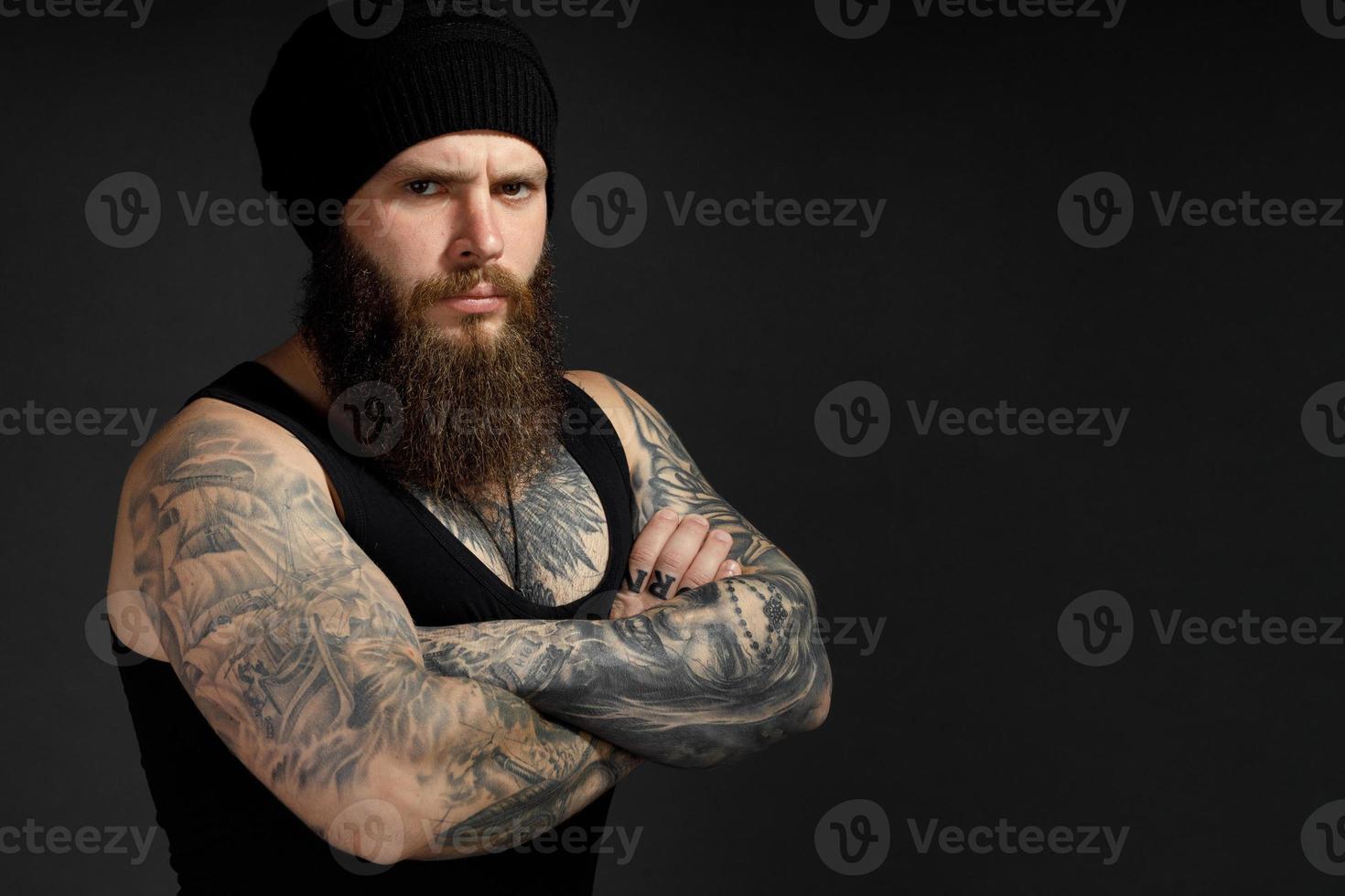 Retrato de un apuesto hombre barbudo con una camiseta negra y un sombrero mirando a la cámara foto