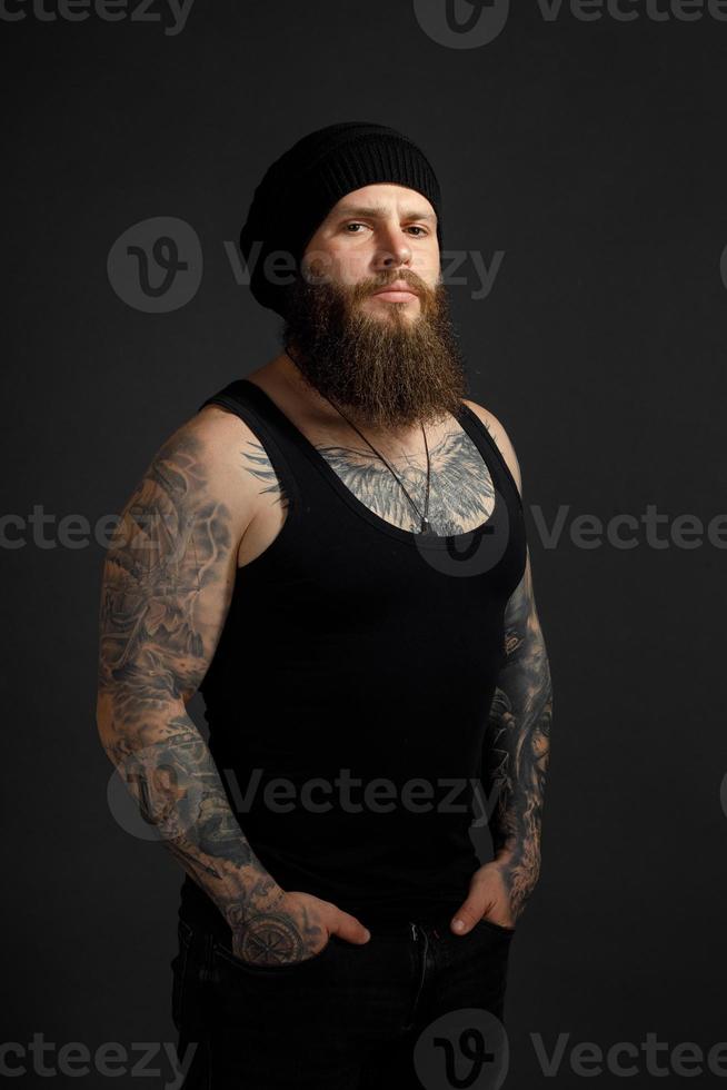 portrait of a handsome bearded man in a black t-shirt and hat looking at the camera photo