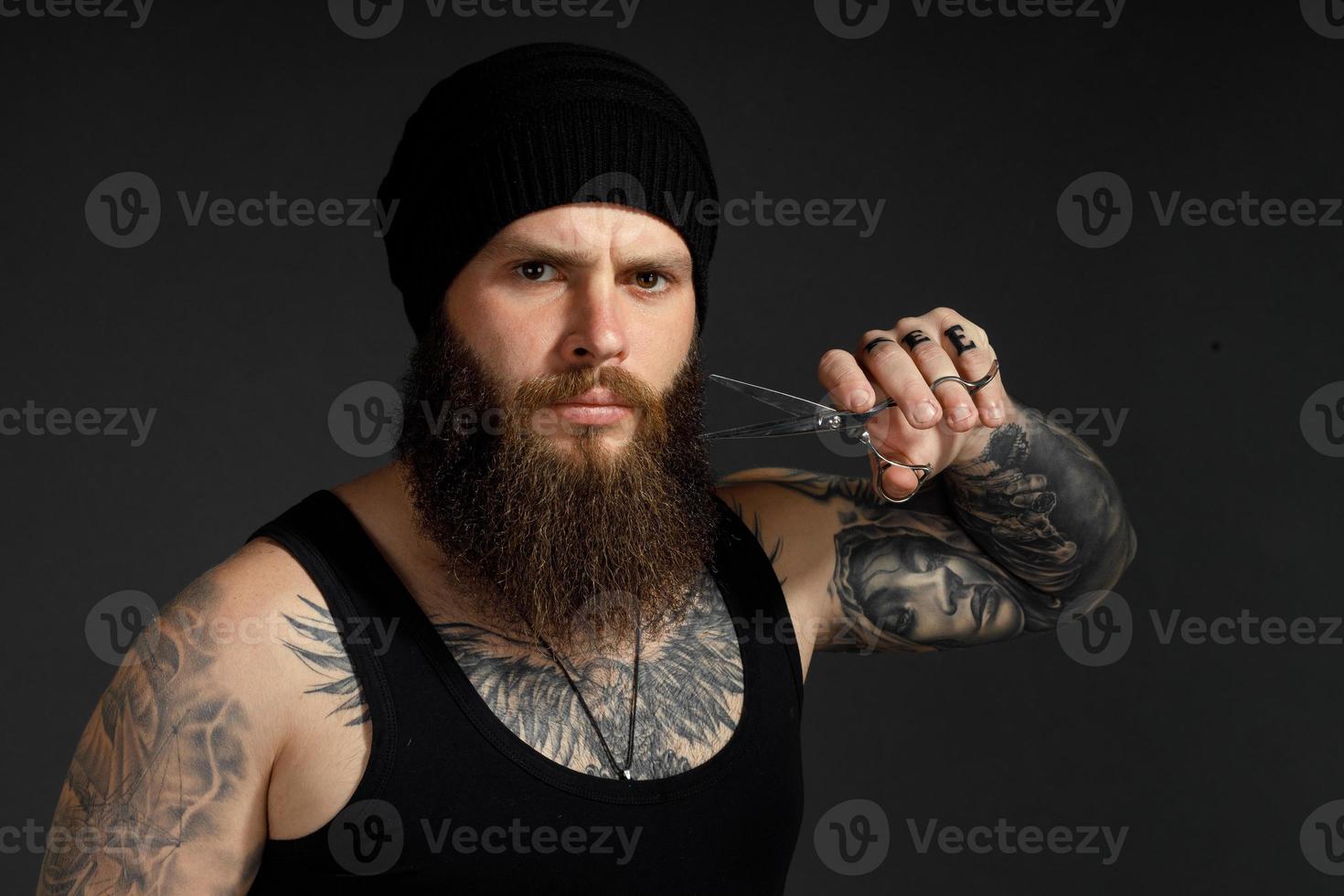 Retrato de un hombre valiente con barba sostiene unas tijeras cerca de su barba y mira a la cámara foto