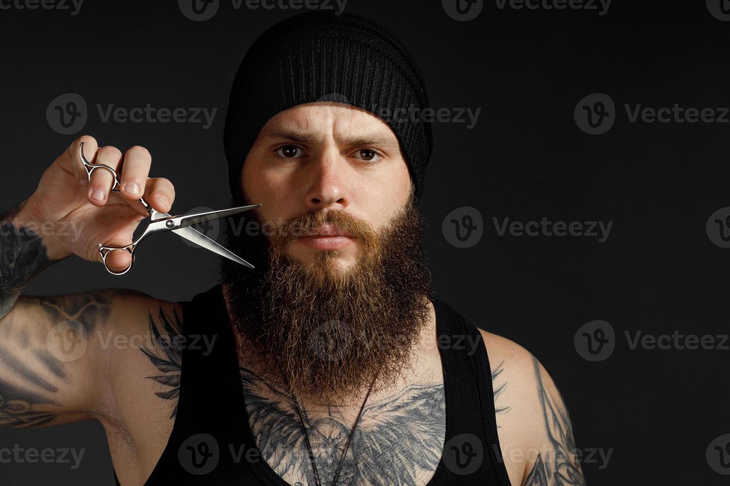 portrait of a courageous man with a beard he holds scissors near his beard and looks at the camera photo