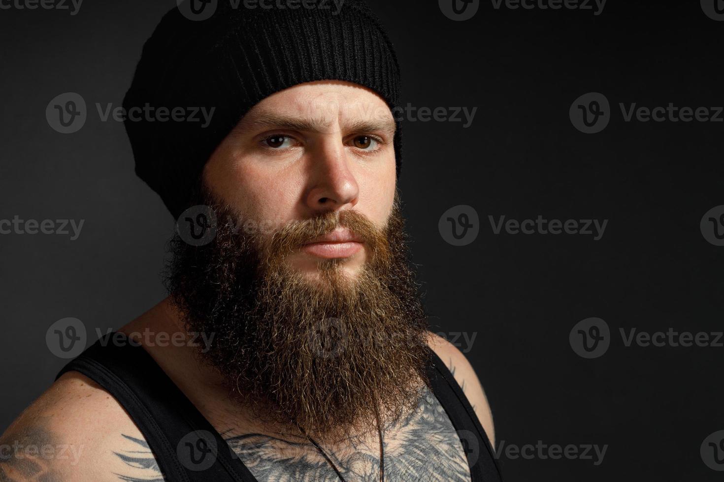 Retrato de un apuesto hombre barbudo con una camiseta negra y un sombrero mirando a la cámara foto