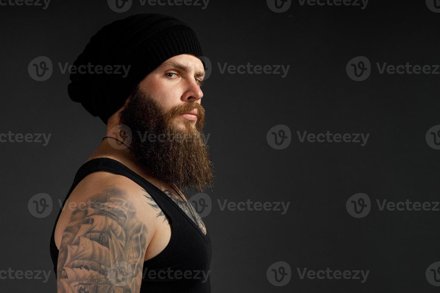 portrait of a handsome bearded man in a black t-shirt and hat looking at the camera photo