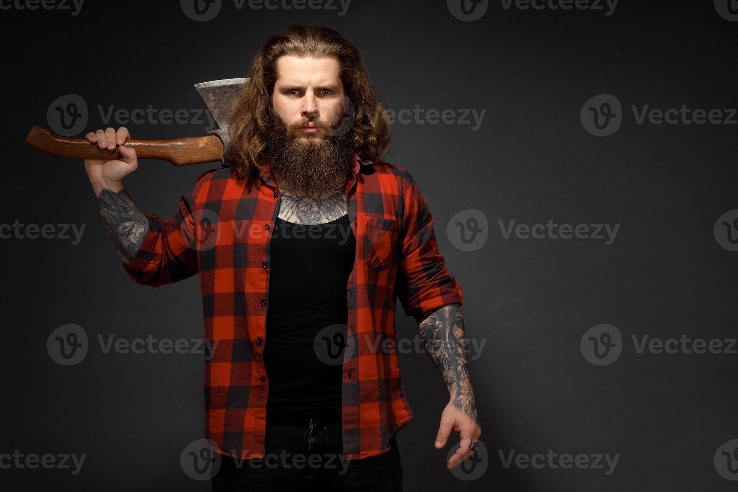 Hombre guapo con cabello largo con un hacha en sus manos sobre un fondo oscuro de estudio foto