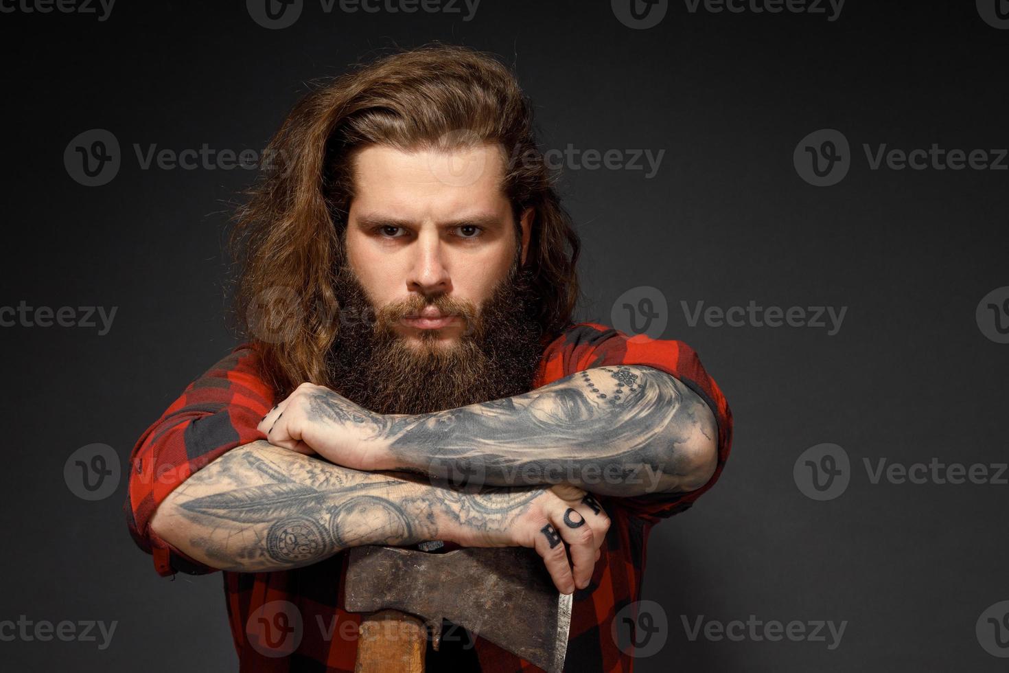 Hombre guapo con cabello largo con un hacha en sus manos sobre un fondo oscuro de estudio foto