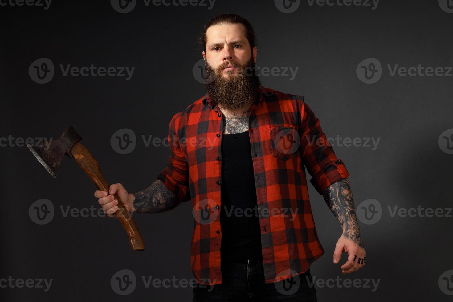 Hombre guapo con cabello largo con un hacha en sus manos sobre un fondo oscuro de estudio foto