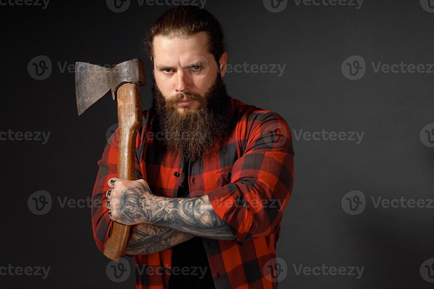 Hombre guapo con cabello largo con un hacha en sus manos sobre un fondo oscuro de estudio foto