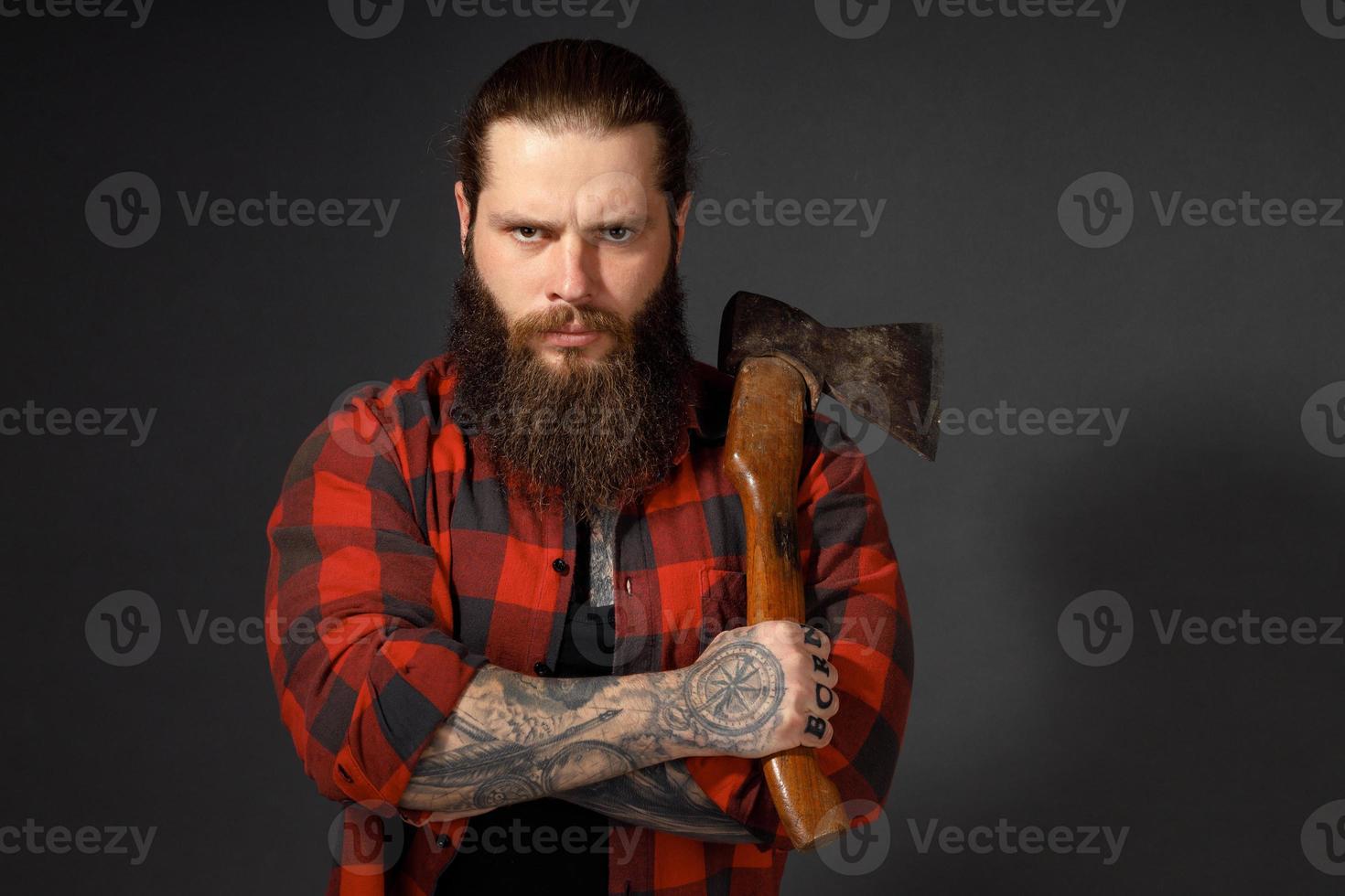 Hombre guapo con cabello largo con un hacha en sus manos sobre un fondo oscuro de estudio foto