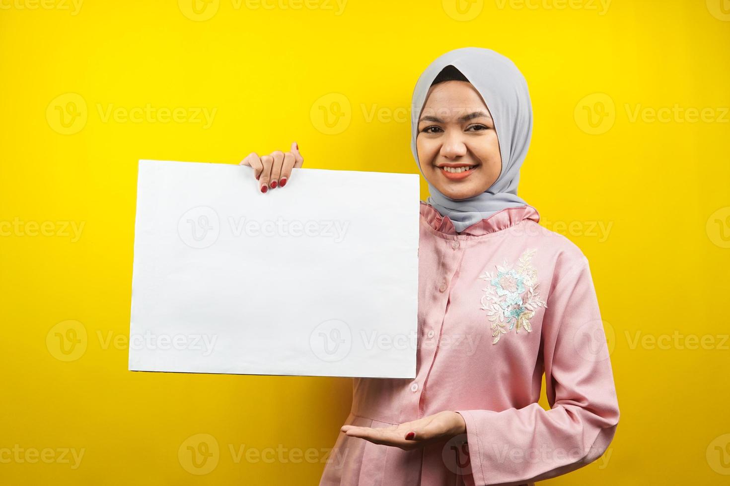 Bastante joven mujer musulmana alegre sosteniendo pancarta vacía en blanco, cartel, tablero blanco, tablero de letrero en blanco, tablero de anuncio blanco, presentando algo en el espacio de la copia, promoción foto