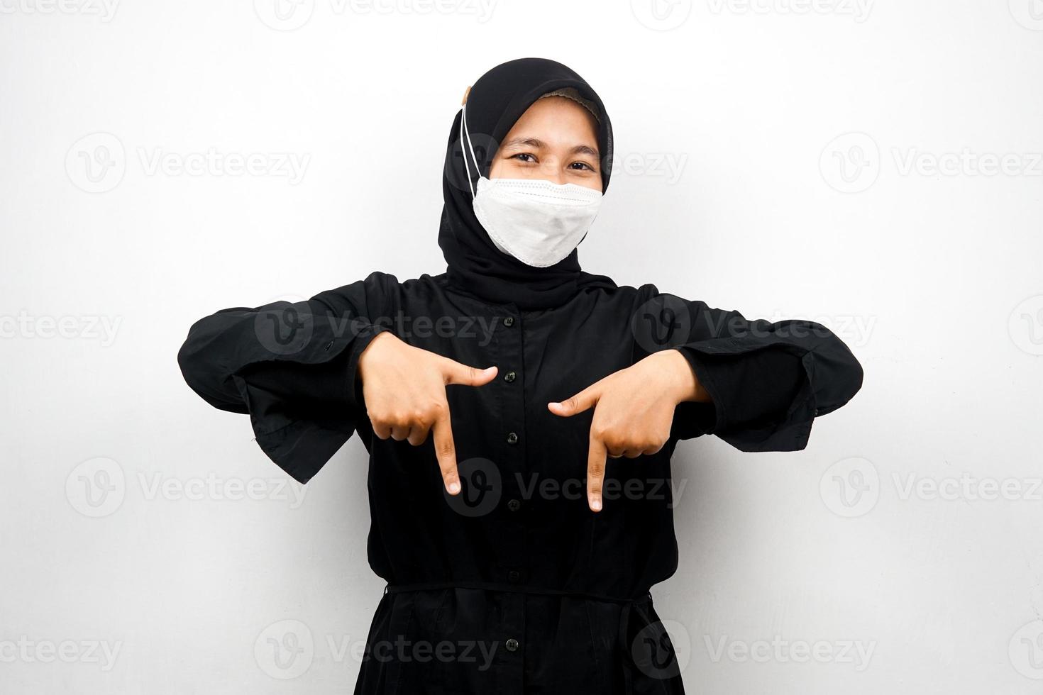 Muslim woman smiling confidently pointing down, presenting something, click the link below, isolated on white background photo