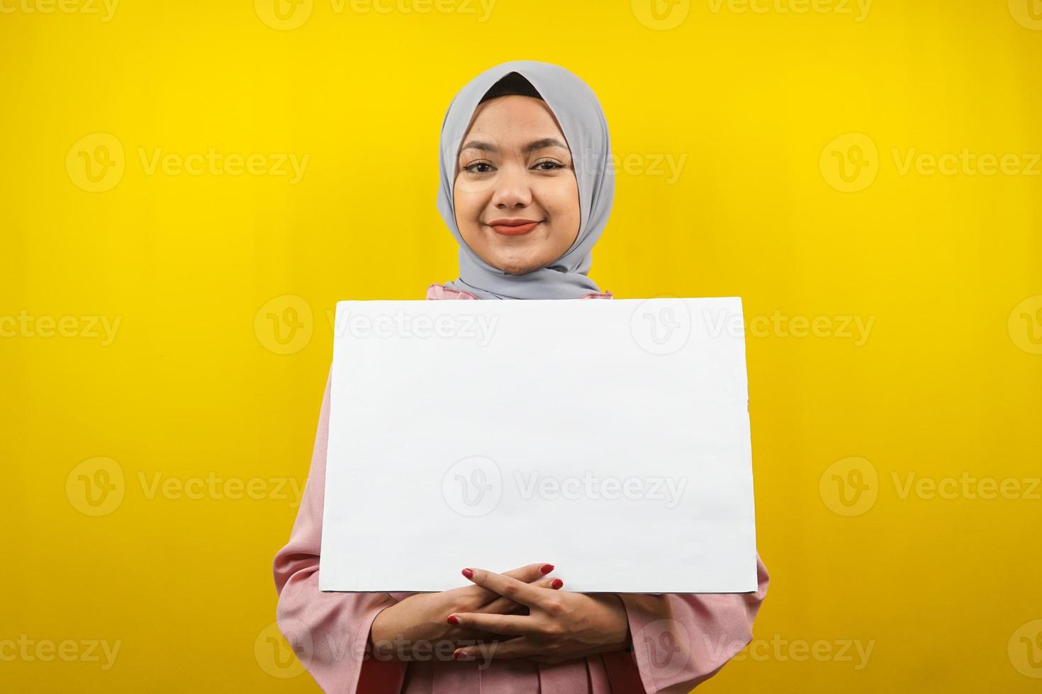 Bastante joven mujer musulmana alegre sosteniendo pancarta vacía en blanco, cartel, tablero blanco, tablero de letrero en blanco, tablero de anuncio blanco, presentando algo en el espacio de la copia, promoción foto