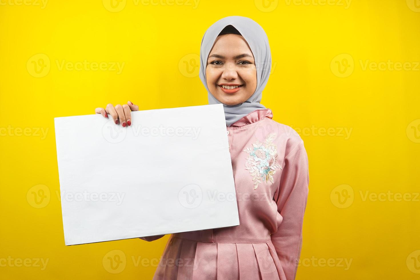 Bastante joven mujer musulmana alegre sosteniendo pancarta vacía en blanco, cartel, tablero blanco, tablero de letrero en blanco, tablero de anuncio blanco, presentando algo en el espacio de la copia, promoción foto