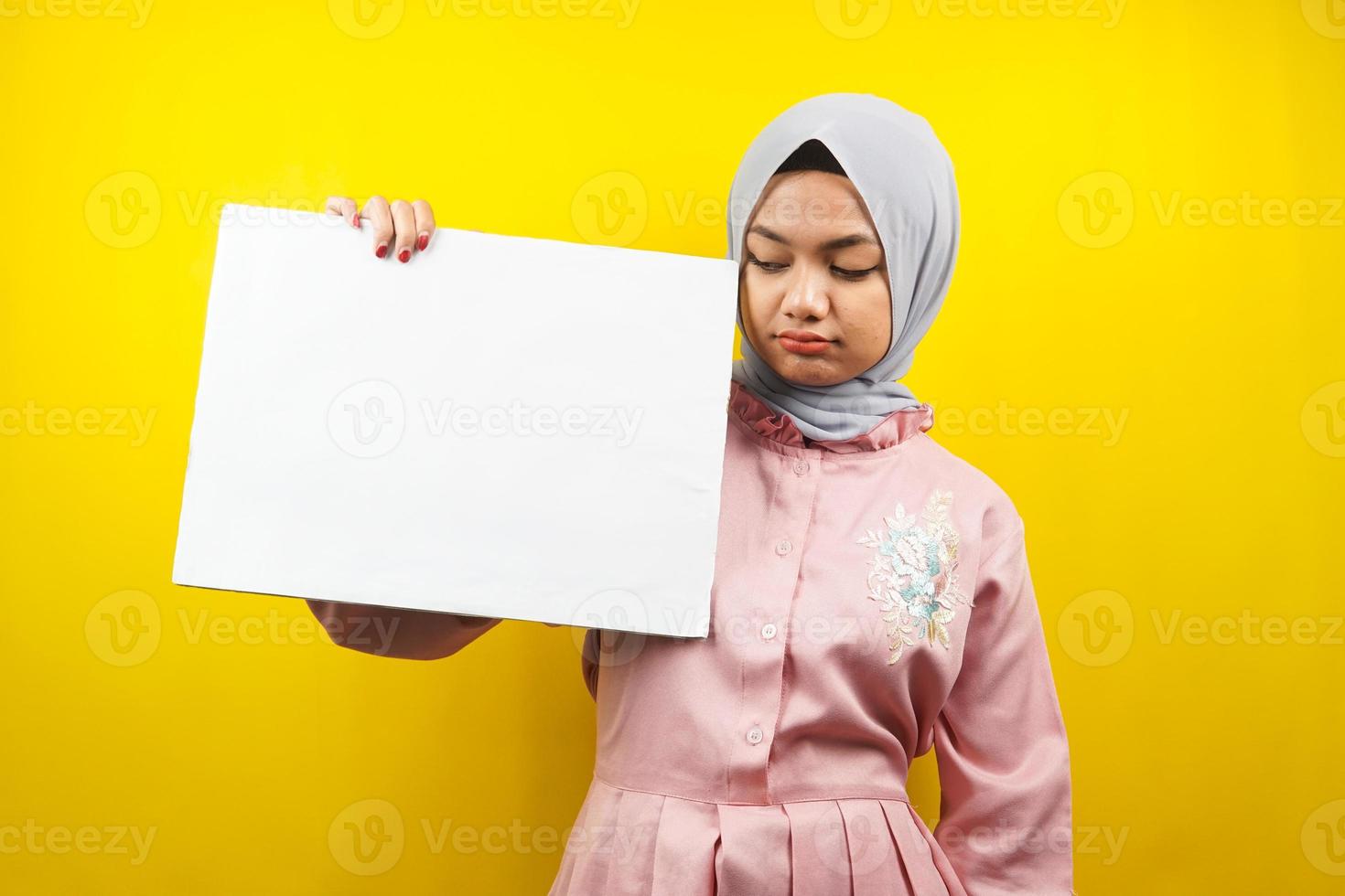 Bastante joven mujer musulmana triste, mano sosteniendo pancarta vacía en blanco, cartel, tablero blanco, tablero de letrero en blanco, tablero de anuncio blanco, presentando algo en el espacio de la copia, promoción foto