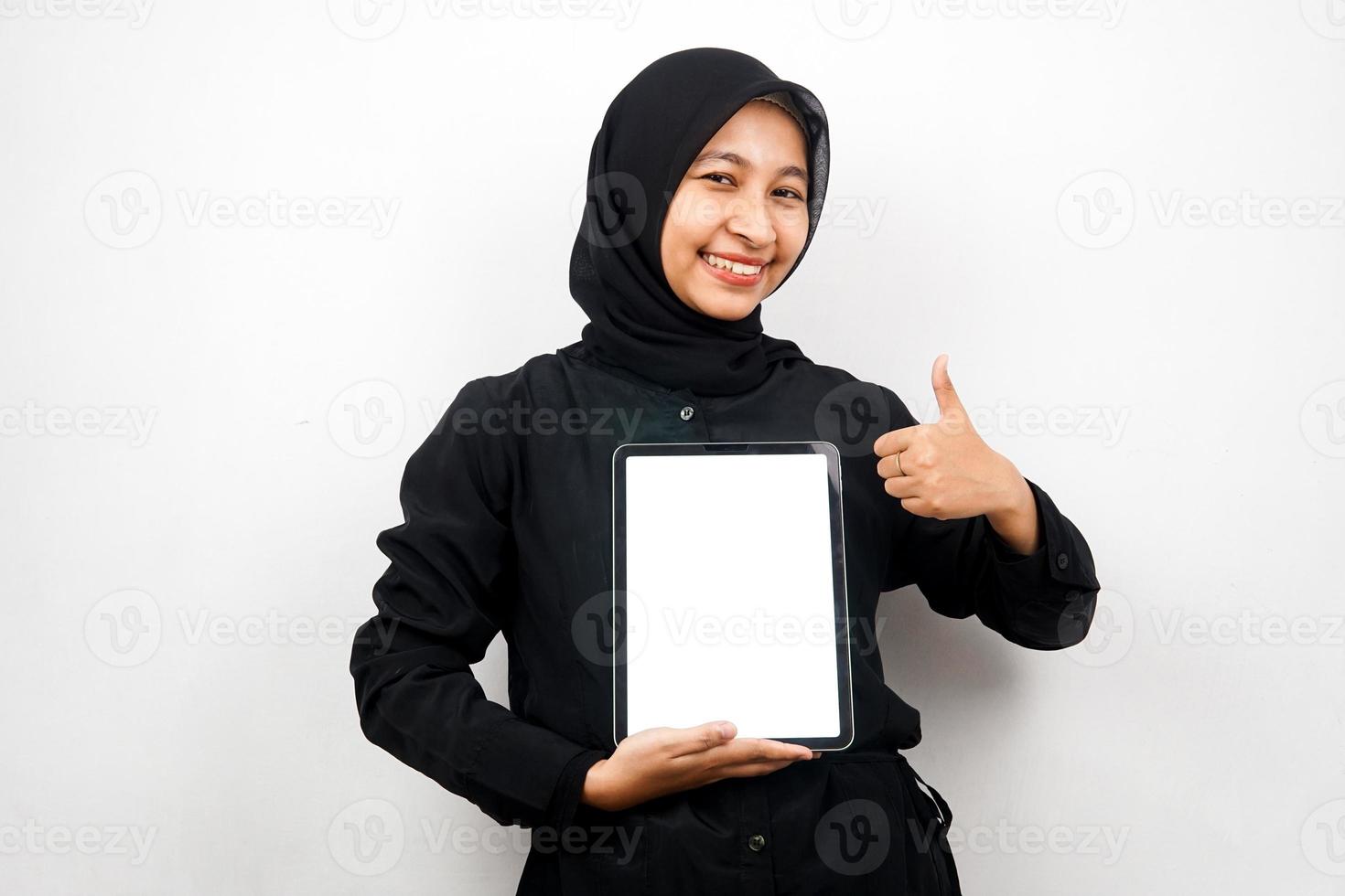 Hermosa joven mujer musulmana asiática sonriendo, tableta de mano con pantalla blanca o en blanco, promoción de aplicaciones, promoción de productos, presentando algo, emocionado y alegre, aislado sobre fondo blanco. foto