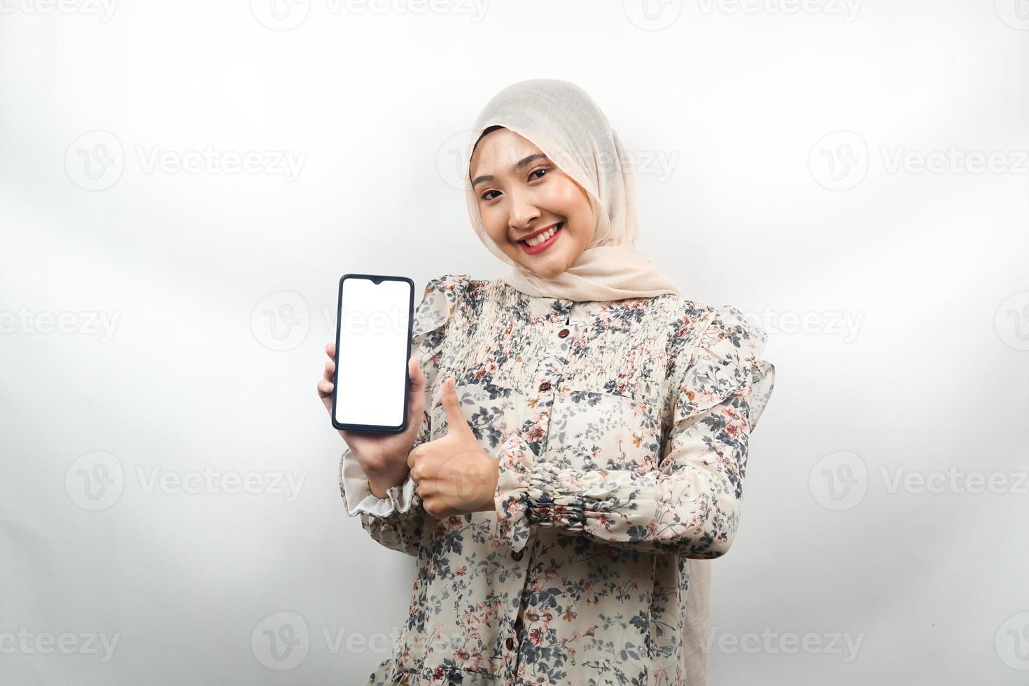 Beautiful young asian muslim woman smiling confidently and excitedly with hands holding smartphone, promoting application, ok sign hand, good job, success, isolated on white background photo